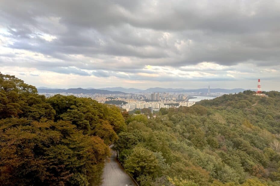 Blick auf eine Stadt mit Bergen im Hintergrund und bewölktem Himmel.