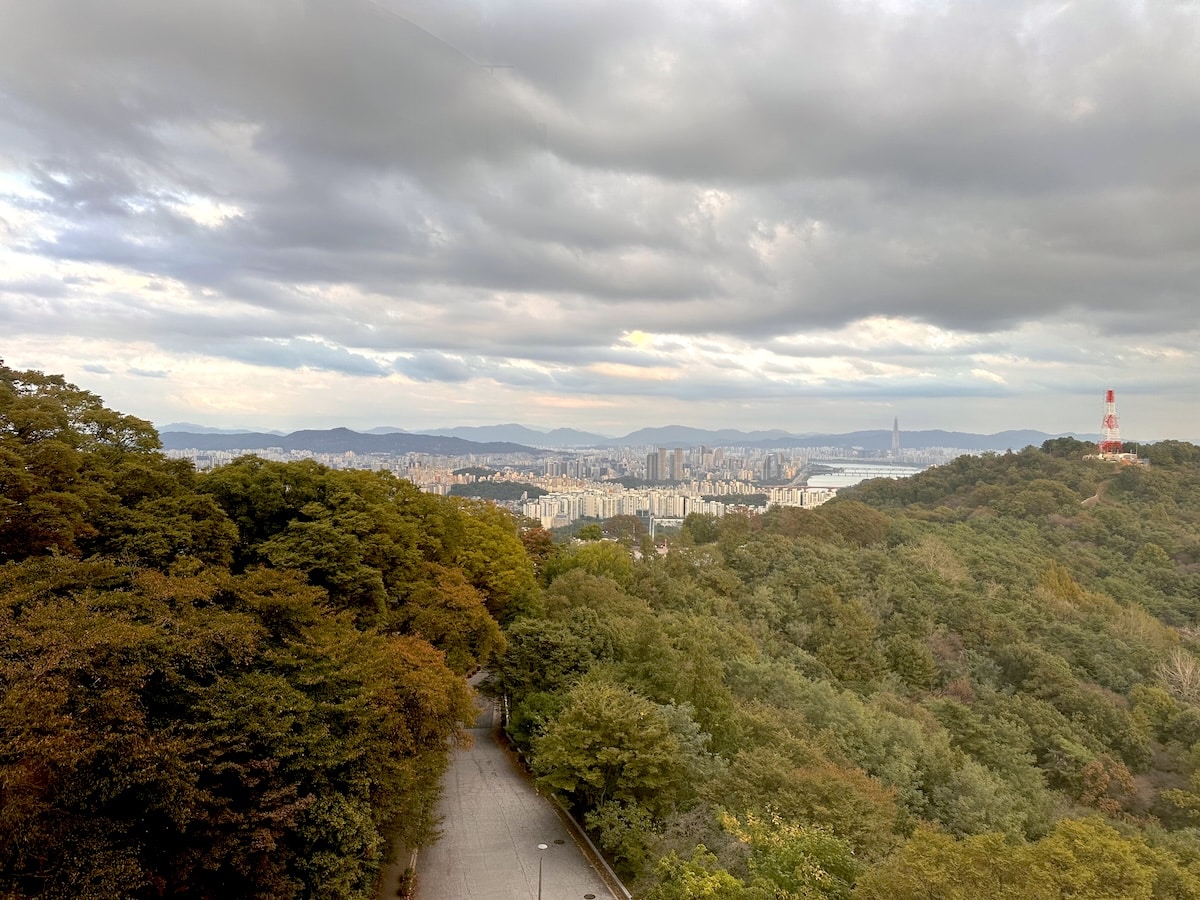 Blick auf eine Stadt mit Bergen im Hintergrund und bewölktem Himmel.