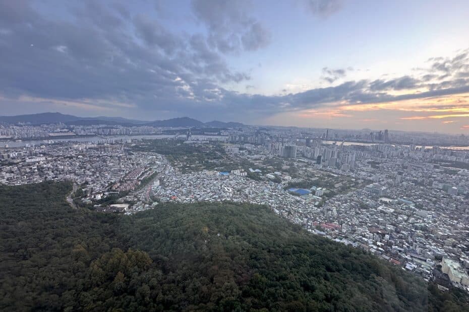Luftaufnahme einer Stadt mit Bergen im Hintergrund und Wolken am Himmel während des Sonnenuntergangs.