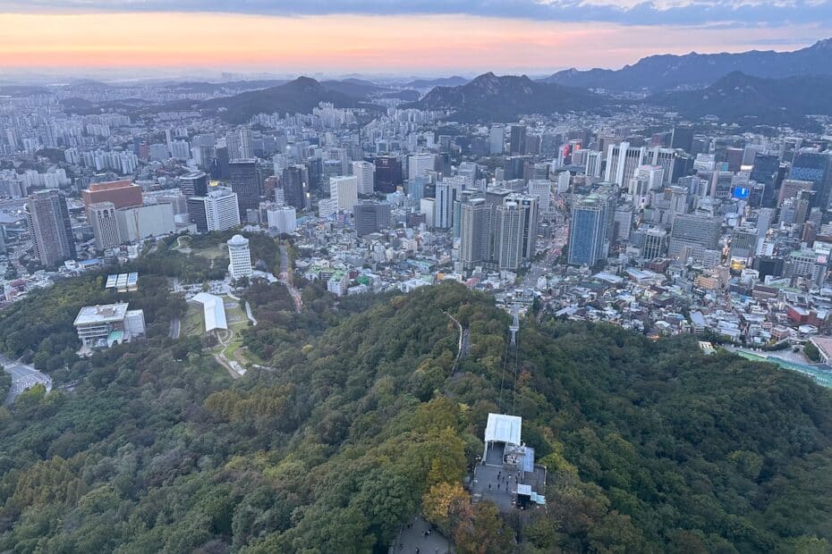 Luftaufnahme von Seoul mit Wolkenkratzern und Bergen im Hintergrund während des Sonnenuntergangs.