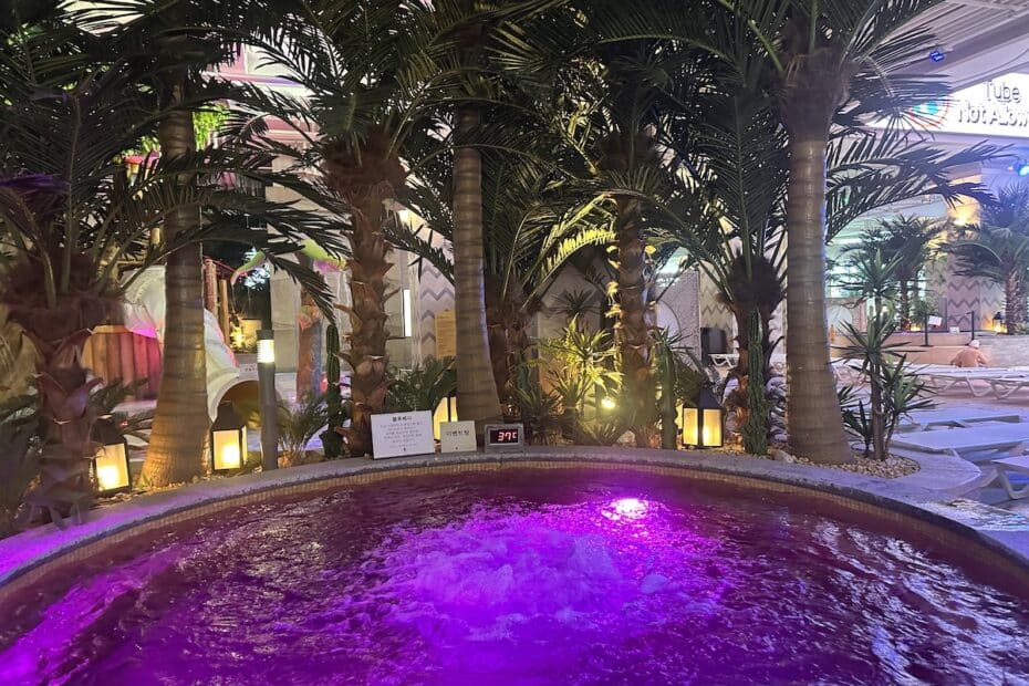 Rundpool mit lila Lichteffekten, umgeben von Palmen und Pflanzen in einem Innenbereich.
