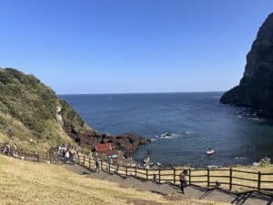 Küstenlandschaft mit Felsen, Wasser und einer kleinen Gruppe von Menschen am Strand.
