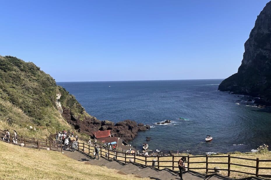 Küstenlandschaft mit Felsen, Wasser und einer kleinen Gruppe von Menschen am Strand.