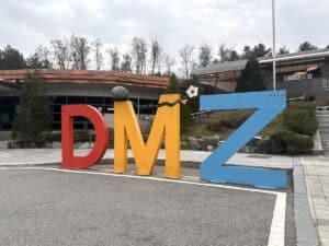 Bunte Skulptur mit den Buchstaben D, M und Z in rot, gelb und blau vor einem Gebäude im Freien.