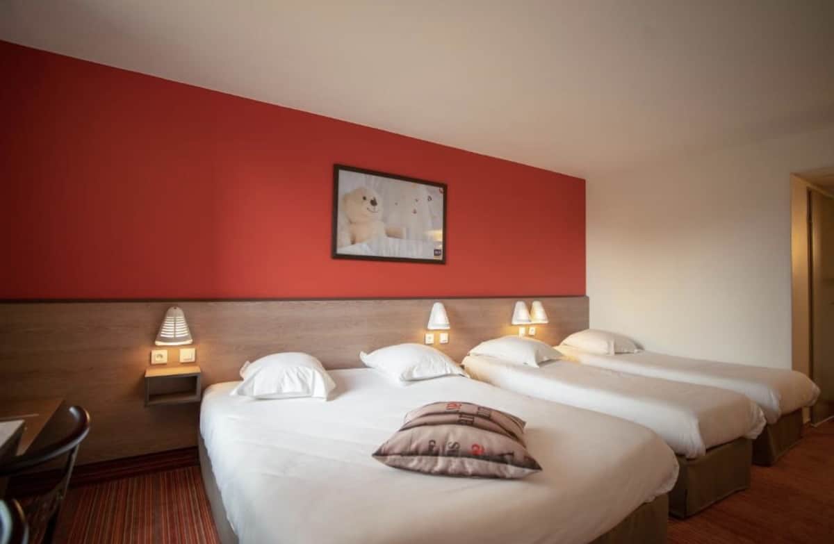 Drei Einzelbetten in einem Hotelzimmer mit roter Wand und modernen Nachttischlampen.