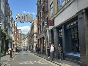Straßenszene in Soho, London mit Menschen und Geschäften, darunter ein Cocktailbar.