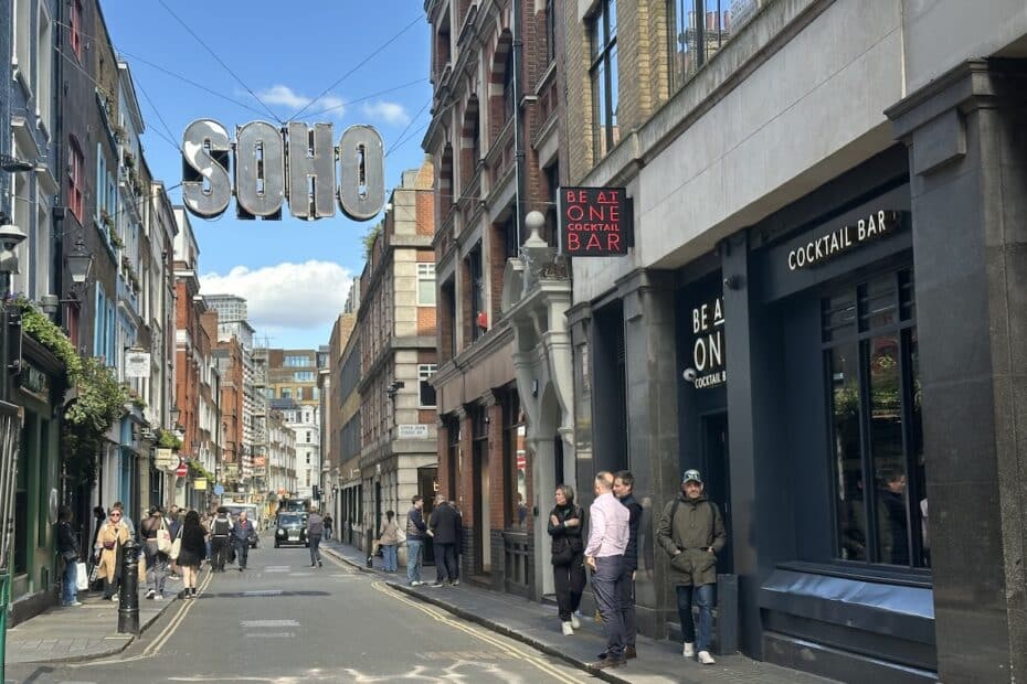Straßenszene in Soho, London mit Menschen und Geschäften, darunter ein Cocktailbar.
