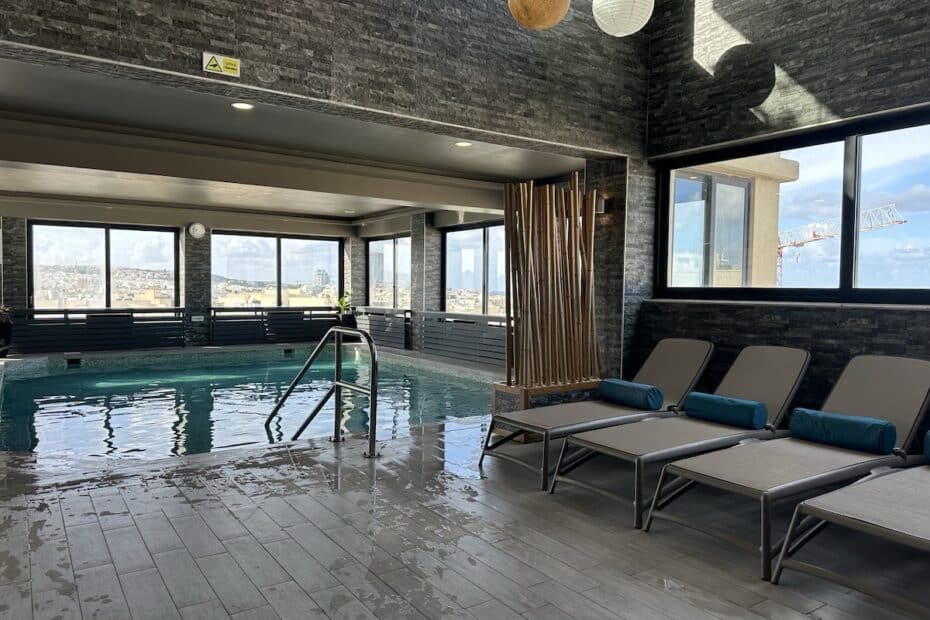 Innenpoolbereich mit modernen Liegen und großen Fenstern, die Tageslicht hereinlassen.
