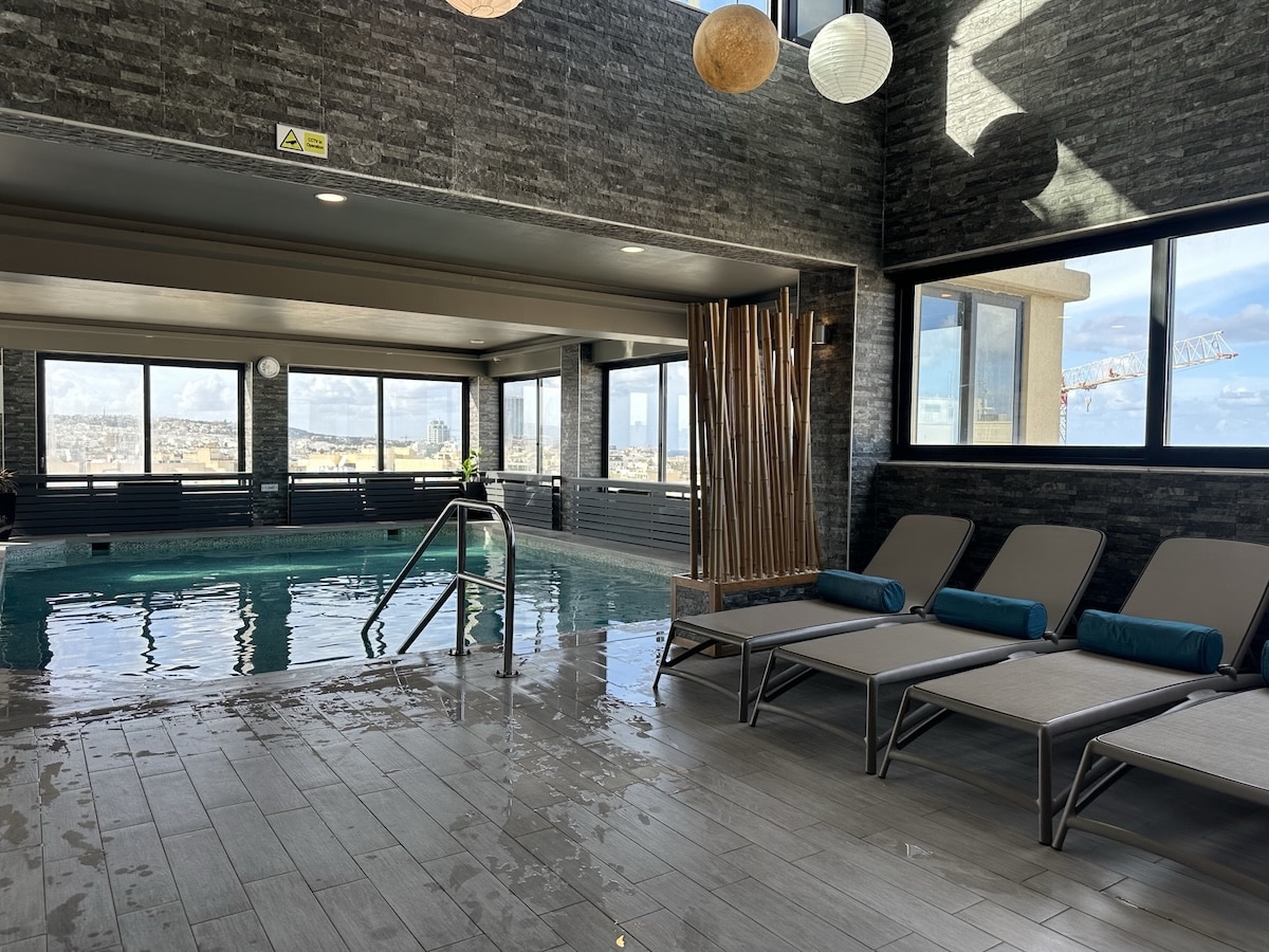 Innenpoolbereich mit modernen Liegen und großen Fenstern, die Tageslicht hereinlassen. AX Victoria Hotel Malta