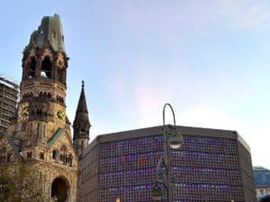 Kaiser-Wilhelm-Gedächtniskirche in Berlin mit einem modernen Gebäude im Vordergrund, beleuchtet in verschiedenen Farben.