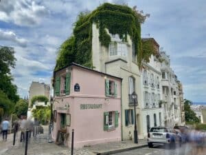 Ein pinkes Restaurant mit grüner Bepflanzung auf dem Dach, umgeben von weißen Gebäuden in einer urbanen Umgebung.