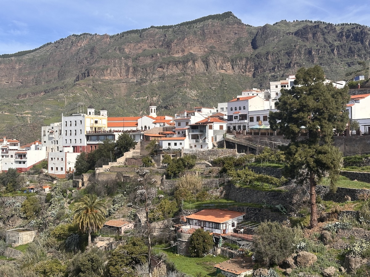 Charmantes Bergdorf Fataga auf Gran Canaria mit weißen Häusern und roten Dächern, terrassierten Gärten vor einer imposanten Berglandschaft; Tejeda und Artenara ragen im Hintergrund auf.