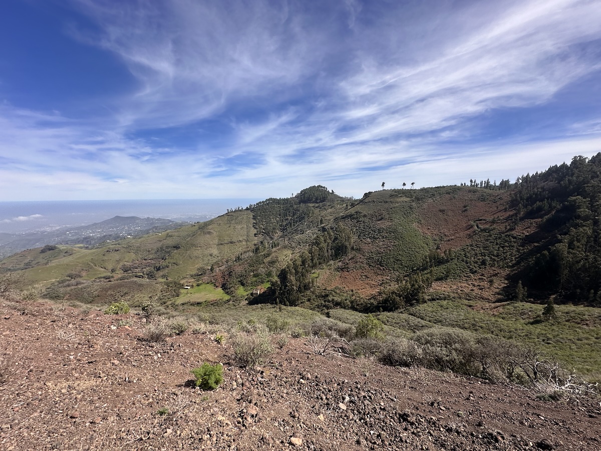 Ausblick über grüne Berglandschaften und rotes Vulkangestein der Insel Gran Canaria mit blauem Himmel; Blick auf Tejeda und Roque Bentayga in einer weiten Berglandschaft.