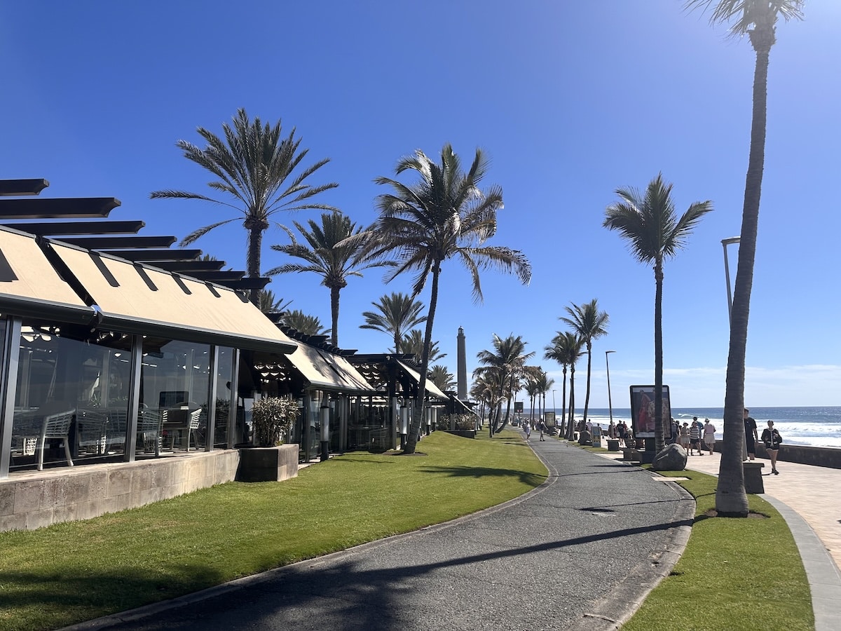 Gran Canaria Innenregion: grüne terrassenförmige Hügel, weißes Dorf am Berghang, Palmen, klare Wolkenbänke im blauen Himmel – Landschaftsaufnahme aus dem Inselinneren
