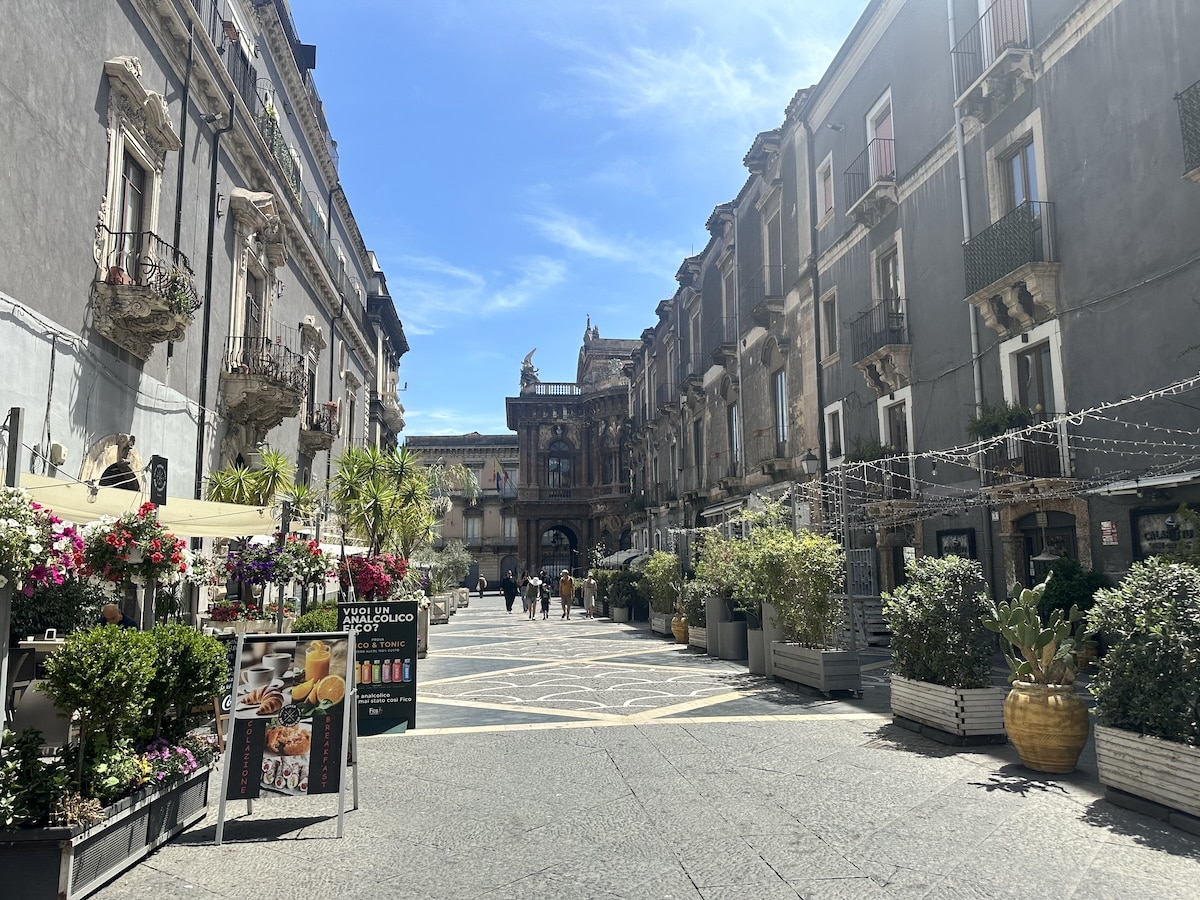 Weite Gasse in Catania zur Piazza del Duomo mit barocken Fassaden, hellgrauem Lavastein, Balkonreihen und sonnigem Himmel