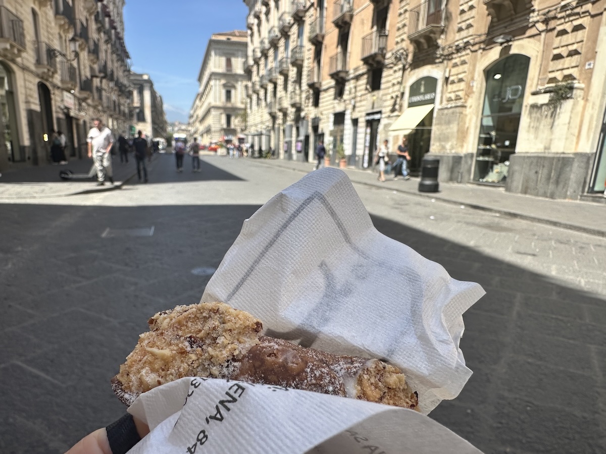 Knusprige, goldbraune Streetfood-Spezialität in weißem Papier an einer belebten Gasse in Catania, mitten im sizilianischen Treiben.
