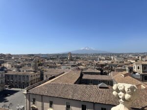 Blick über Catania mit roten Ziegeldächern und dem schneebedeckten Ätna am Horizont, klarer Himmel und typisch sizilianische Altstadt-Atmosphäre für deinen Tag.