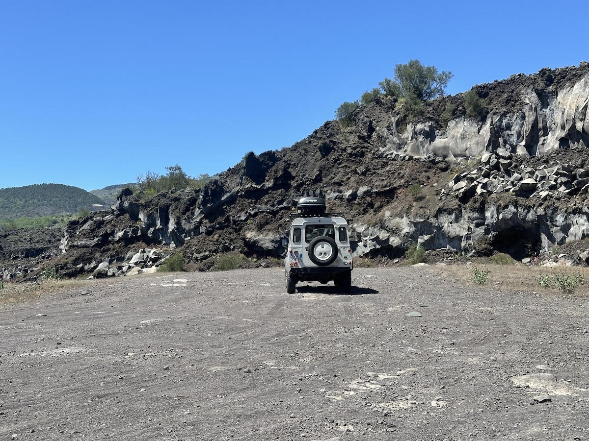Jeep auf einer steinigen Offroad-Strecke vor schwarz-grauen Felswänden am Ätna, während die Ätna Jeep Tour ab Catania die Vulkanlandschaft zeigt.