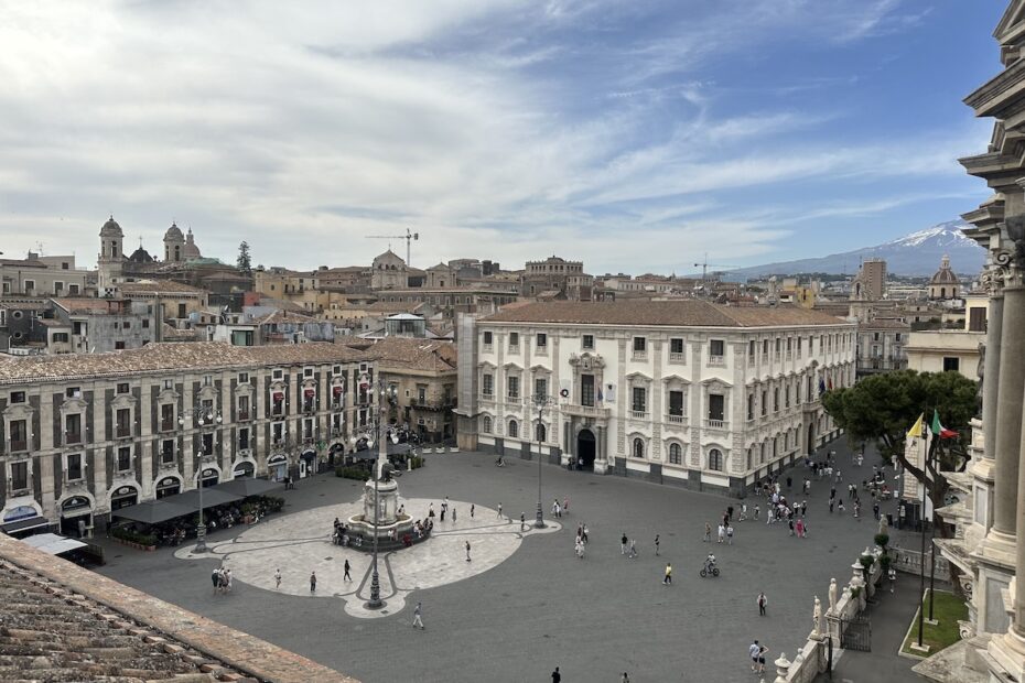 Blick über Catania auf den Piazza del Duomo im Centro Storico, mit Kuppeln über den Altstadt-Gebäuden, wolkigem Himmel und hellem Tageslicht.