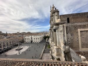 Im Blick auf Piazza del Duomo in Catania ragen steinerne graue Säulen aus dem Teatro Romano in den Himmel, mit weitem Platz und Wolken über der Altstadt.
