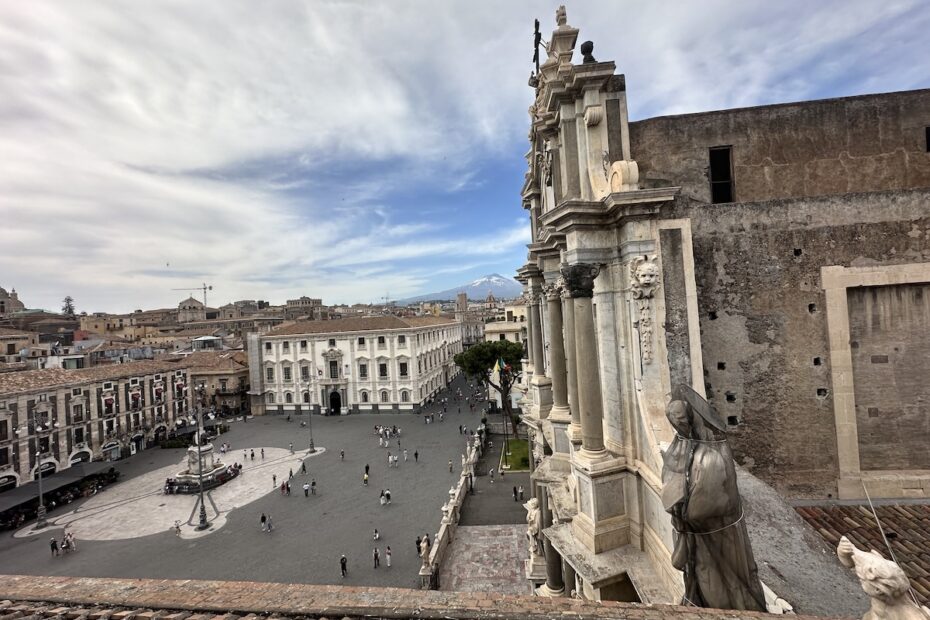Im Blick auf Piazza del Duomo in Catania ragen steinerne graue Säulen aus dem Teatro Romano in den Himmel, mit weitem Platz und Wolken über der Altstadt.
