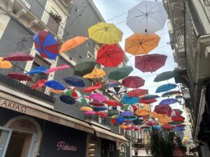 Bunte, hängende Regenschirme über der Gasse in Catania mit Blick auf die Altstadt-Stimmung, typisch für Märkte und Streetfood-Tipps rund um den Ätna.