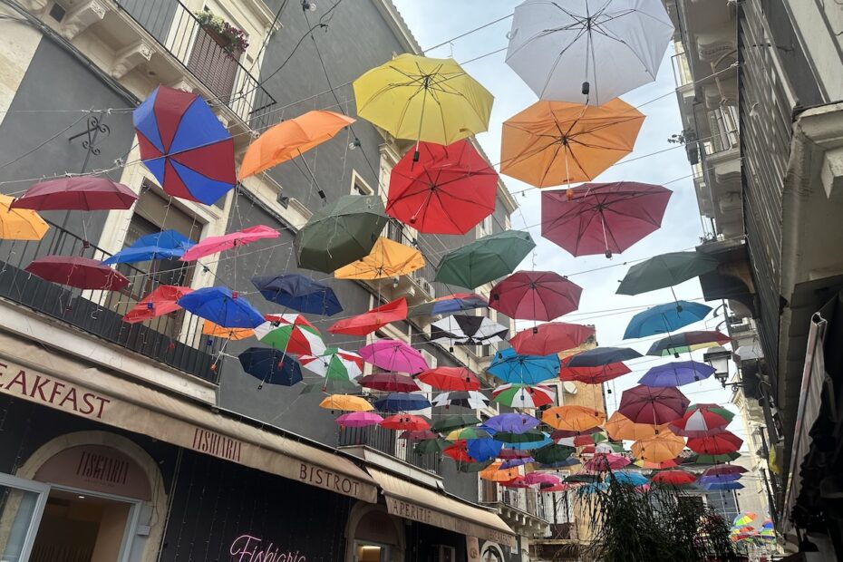Bunte, hängende Regenschirme über der Gasse in Catania mit Blick auf die Altstadt-Stimmung, typisch für Märkte und Streetfood-Tipps rund um den Ätna.