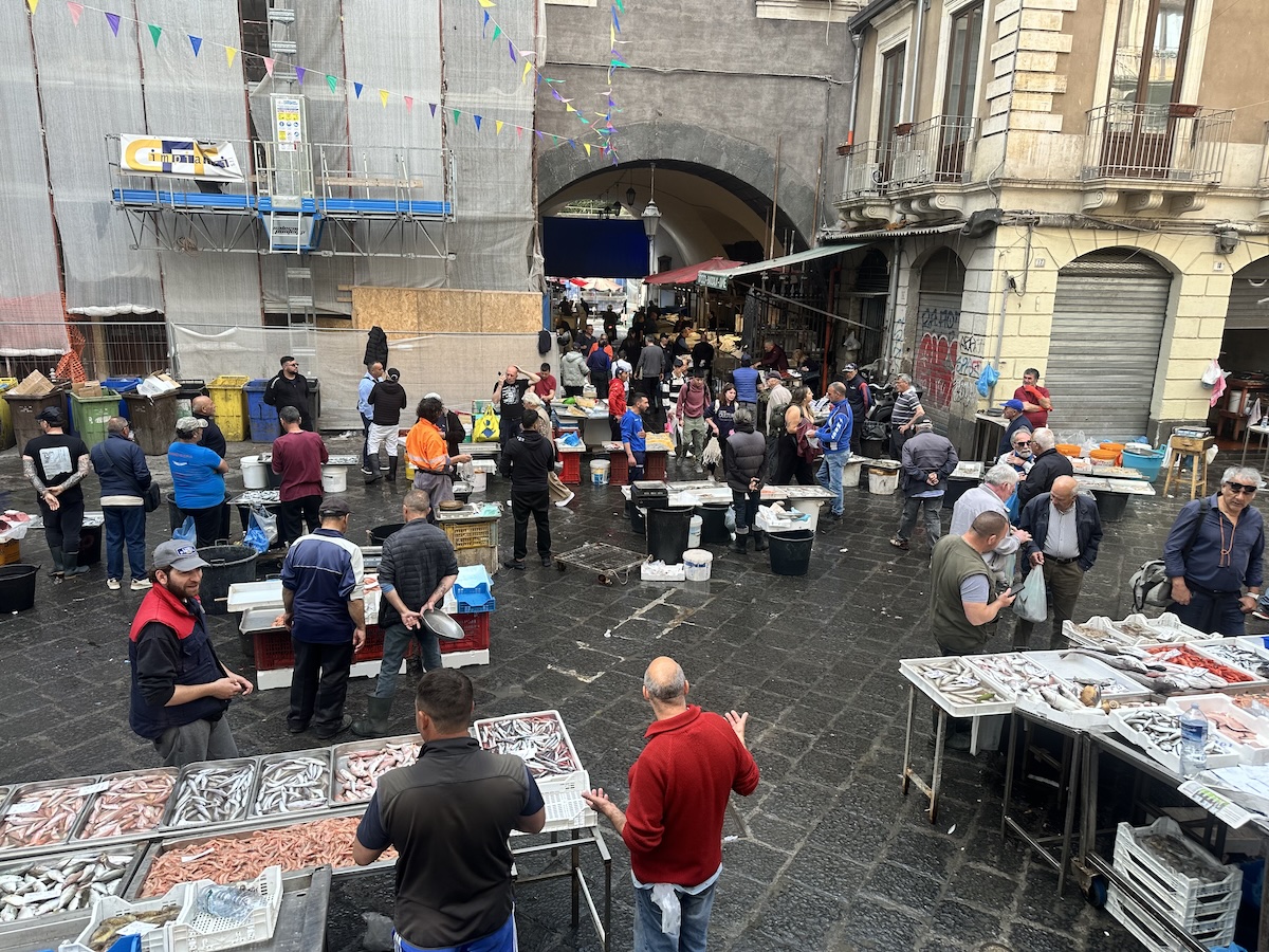 Auf dem Fischmarkt La Pescheria in Catania herrscht lebendige Marktstimmung: viele Menschen zwischen Fischkisten, überdachte Gänge und dunkler Lavastein.