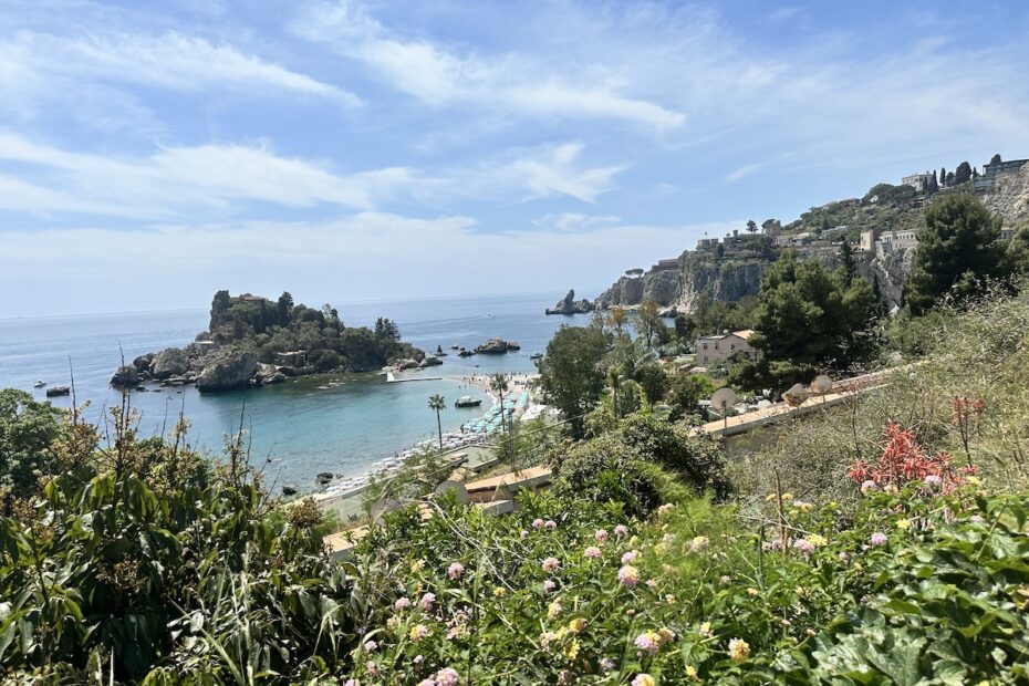 Blick von den Hügeln bei Taormina auf türkisblaues Meer und Isola Bella, mit Küste, Buchten und grünen Gärten unter blauem Himmel.