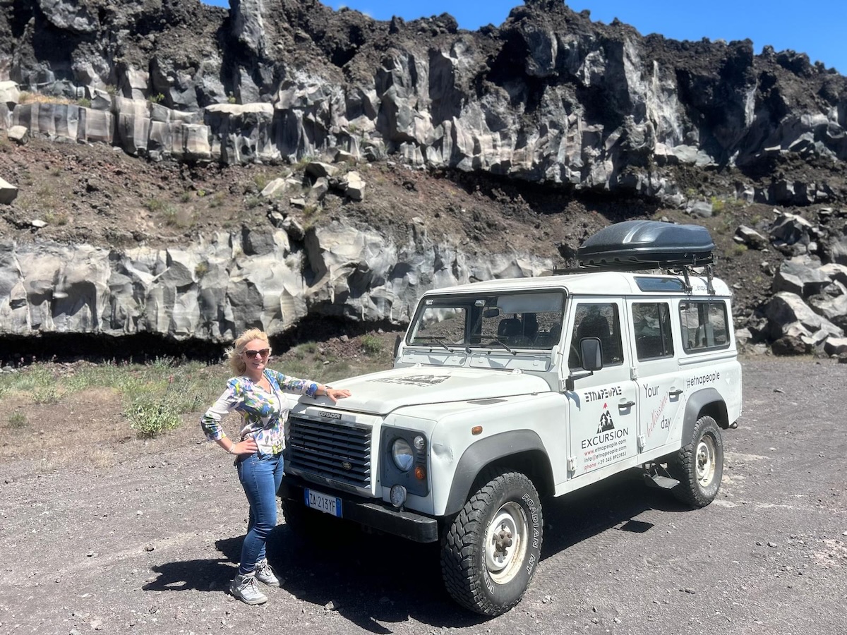 Bei einer Jeep Tour am Ätna steht ein weißes Geländefahrzeug vor vulkanischen Felsen; im Hintergrund eine dunkle Kraterwand rund um Catania.
