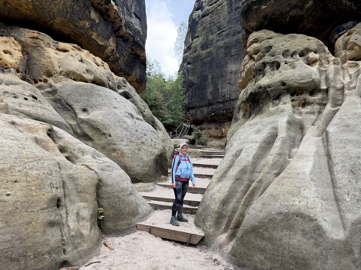 Eine Wanderin steht zwischen hohen Sandsteinfelsen auf den Stufen des Malerwegs 4 in der Sächsischen Schweiz nahe der Schrammsteinaussicht.
