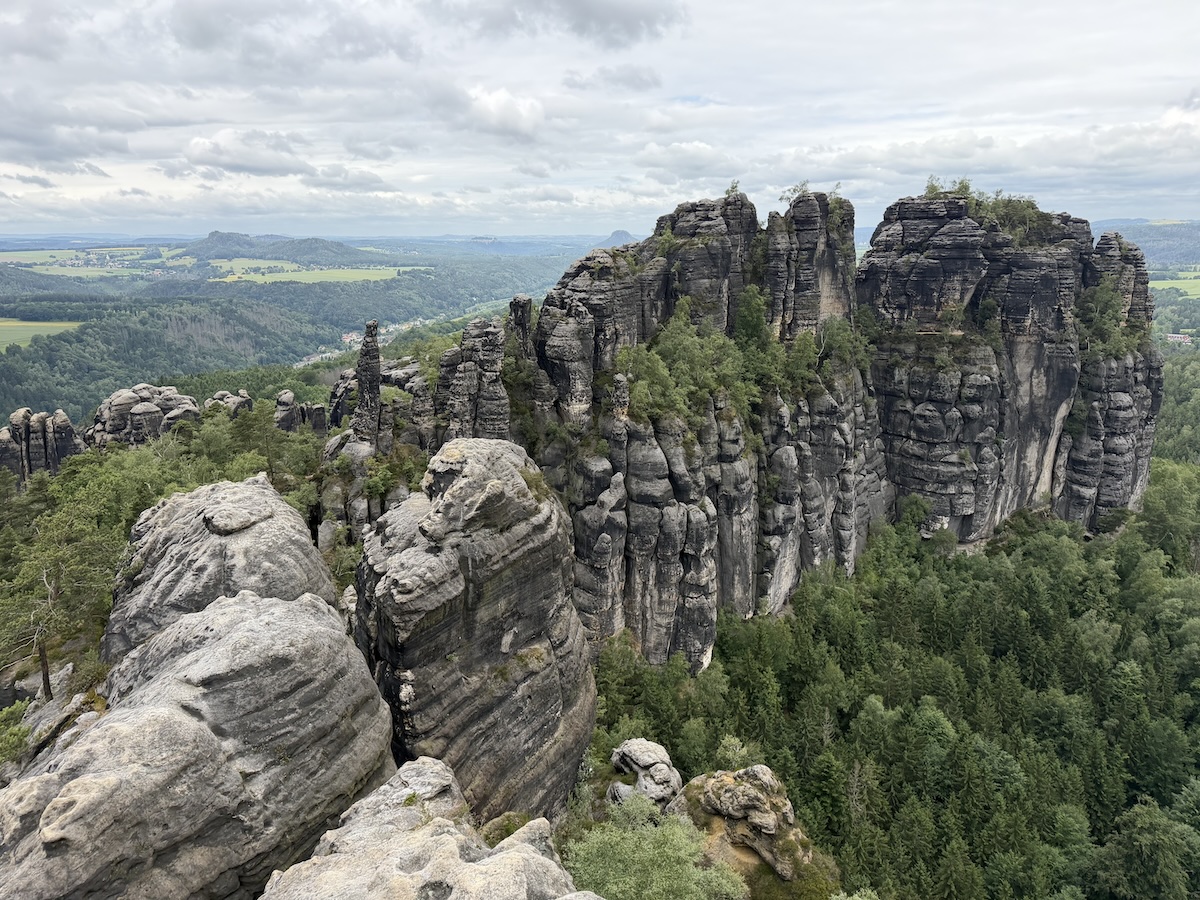 Von der Schrammsteinaussicht öffnet sich ein weiter Blick über markante Sandsteinfelsen, dichte Wälder und die sanfte Landschaft der Sächsischen Schweiz.