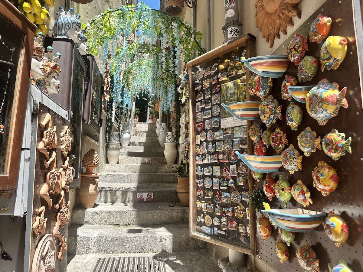 Zwischen bunten Keramikfischen und Souvenirs führt eine steinerne Treppe hinauf durch die Altstadt von Taormina auf Sizilien.