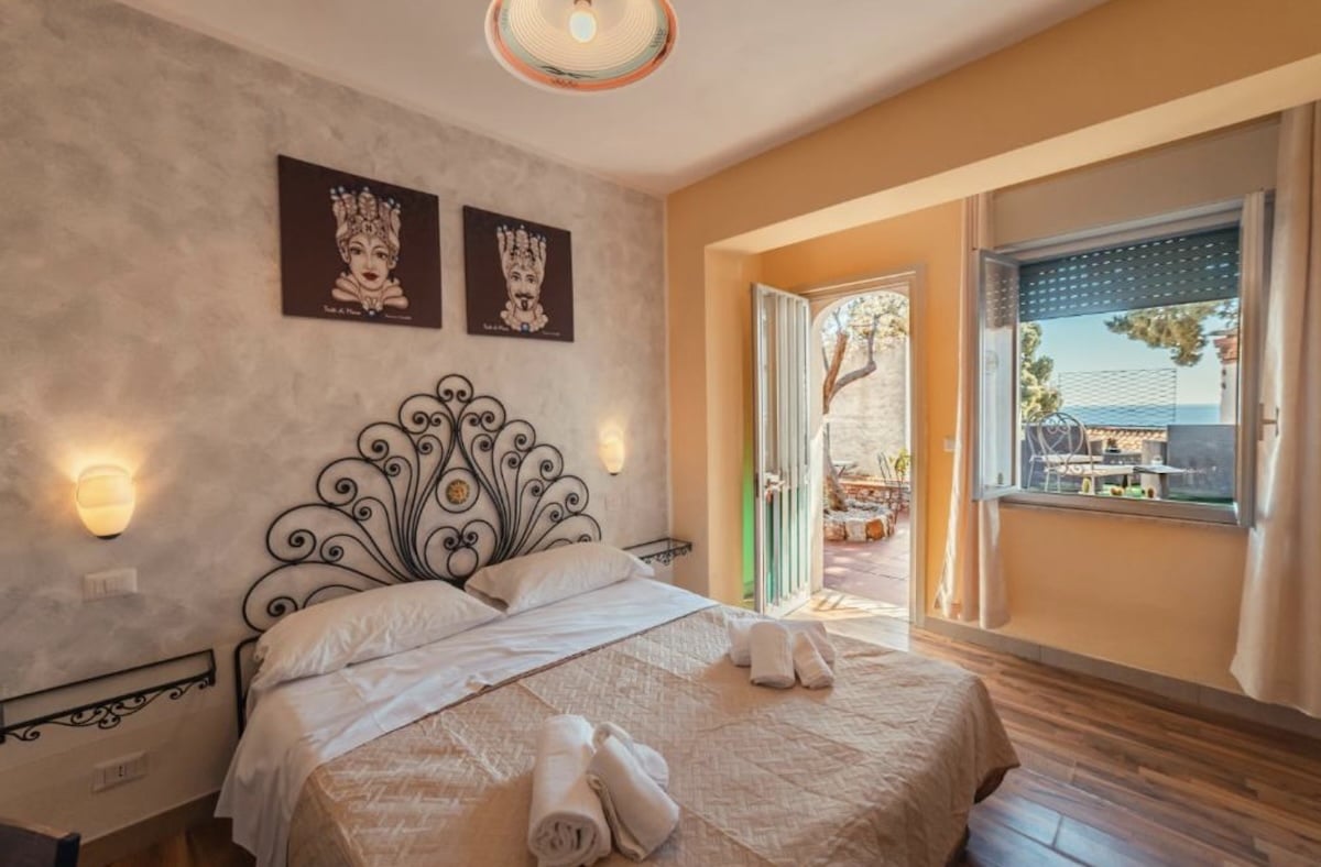 In Taormina öffnet ein gemütliches Hotelzimmer den Blick auf Meer und Balkon, mit dekorativem Kopfteil, heller Einrichtung und warmen Tönen.