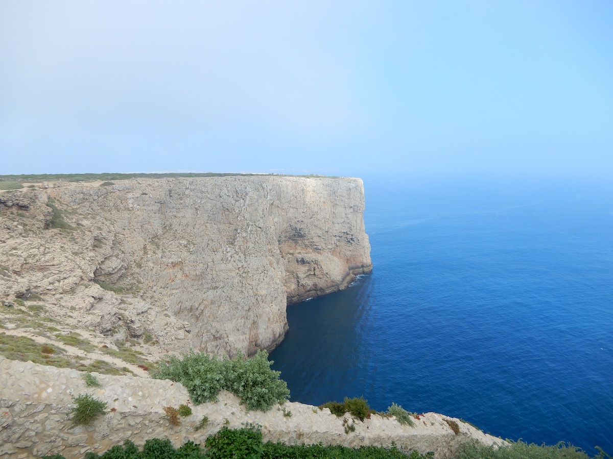 Hohe Kalkklippen fallen an der Algarve ins tiefblaue Meer, während feiner Küstenbewuchs den Rand säumt.