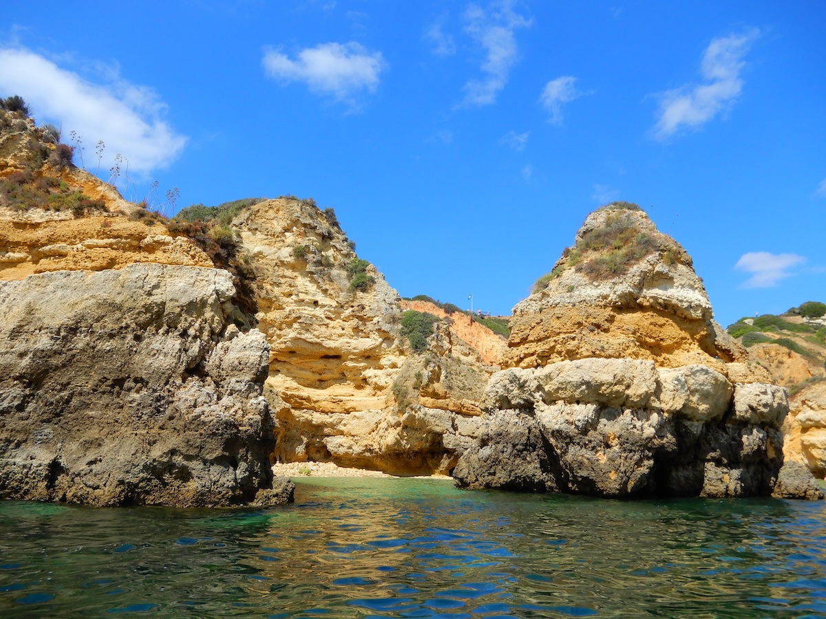 Hohe Kalksteinfelsen ragen aus dem türkisgrünen Meer an der Küste von Lagos an der Algarve unter blauem Himmel auf.