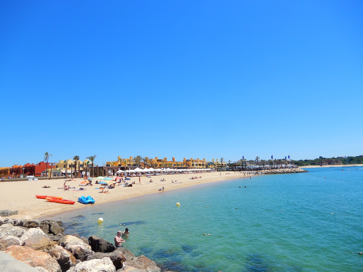 Ein sonniger Sandstrand von Portimão an der Algarve mit klarem türkisfarbenem Wasser, Badegästen und bunten Kajaks am Ufer.