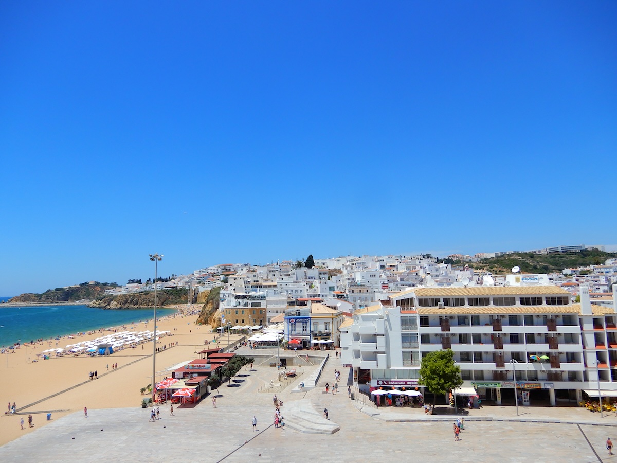 Über den breiten Sandstrand von Albufeira an der Algarve blicken weiße Häuser und Hotels bis zur Küste hinunter.