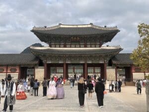 Vor dem Gyeongbokgung Palace in Seoul stehen viele Besucher, einige in farbenfrohen Hanbok, unter einem großen traditionellen Tor.