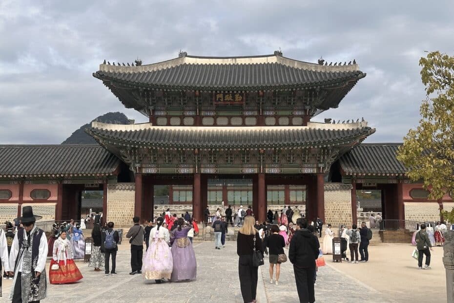 Vor dem Gyeongbokgung Palace in Seoul stehen viele Besucher, einige in farbenfrohen Hanbok, unter einem großen traditionellen Tor.