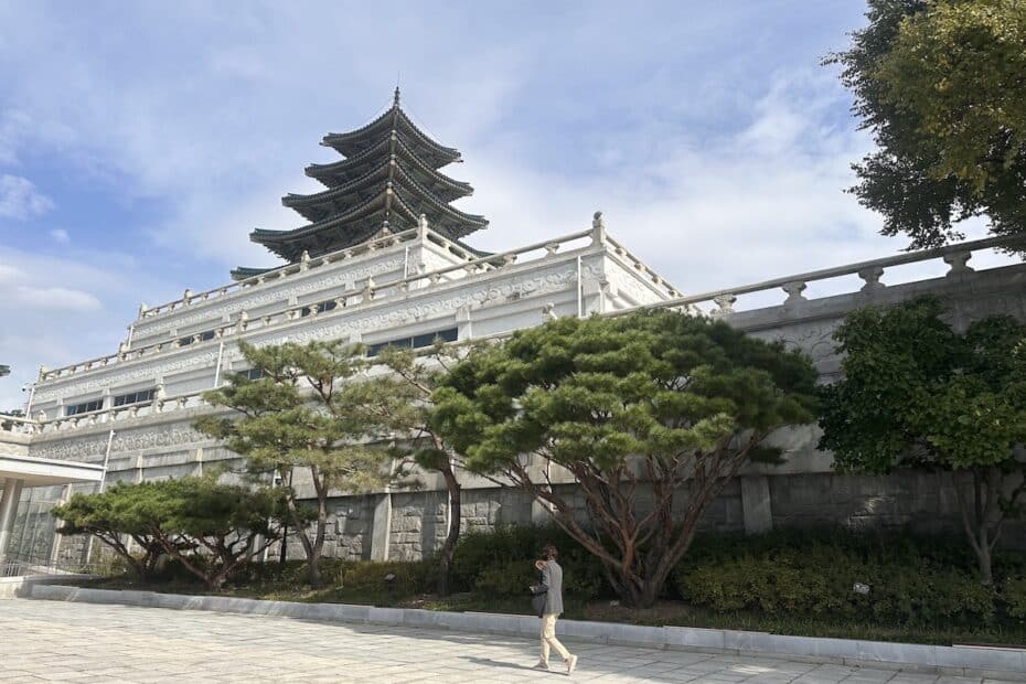 Vor dem Gyeongbokgung Palast in Seoul erhebt sich eine mehrstöckige Pagode über der weißen Mauer, während ein Besucher über den Hof geht.