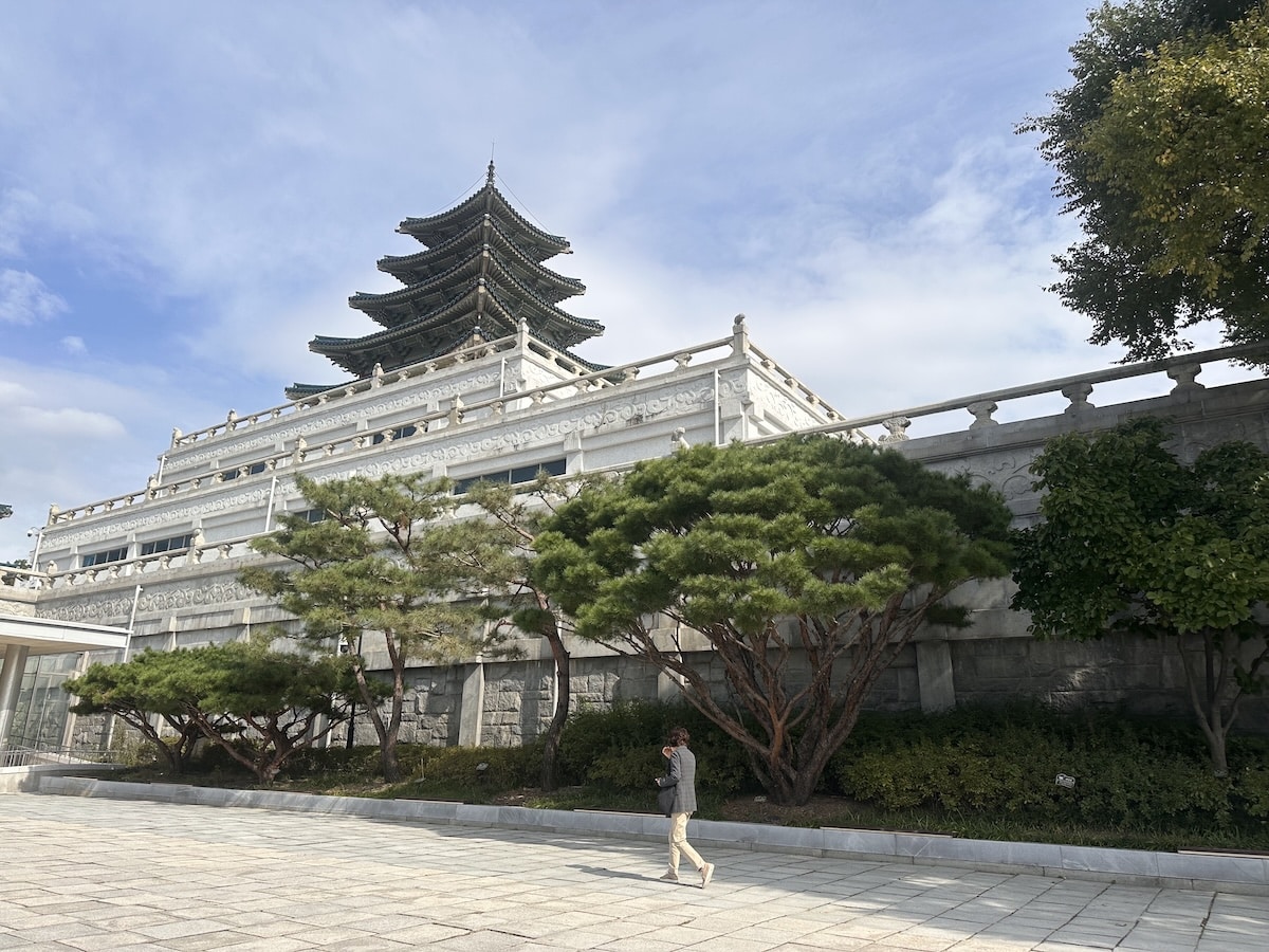 Vor dem Gyeongbokgung Palast in Seoul erhebt sich eine mehrstöckige Pagode über der weißen Mauer, während ein Besucher über den Hof geht.