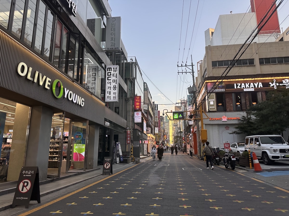 Eine belebte Straße in Seoul mit Olive Young, Izakaya-Schildern und Spaziergängern zwischen Geschäften in der Abenddämmerung in Südkorea.