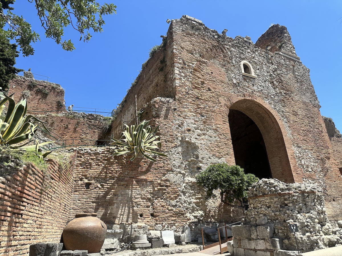 Im Teatro Antico Taormina ragen alte Backsteinmauern und ein großer Torbogen unter klarem Himmel auf.