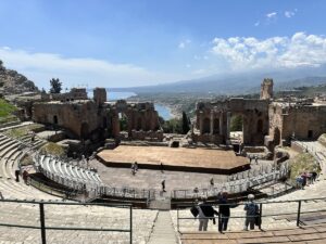 Im Teatro Antico Taormina öffnen sich die Ruinen zum Meer und zum Ätna, während Besucher auf den Rängen stehen.
