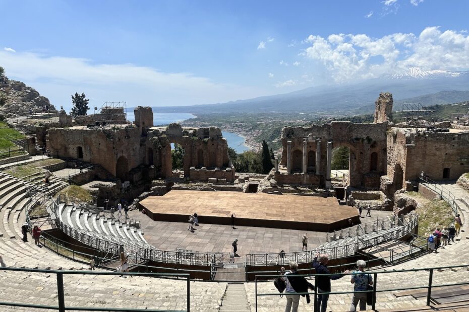 Im Teatro Antico Taormina öffnen sich die Ruinen zum Meer und zum Ätna, während Besucher auf den Rängen stehen.