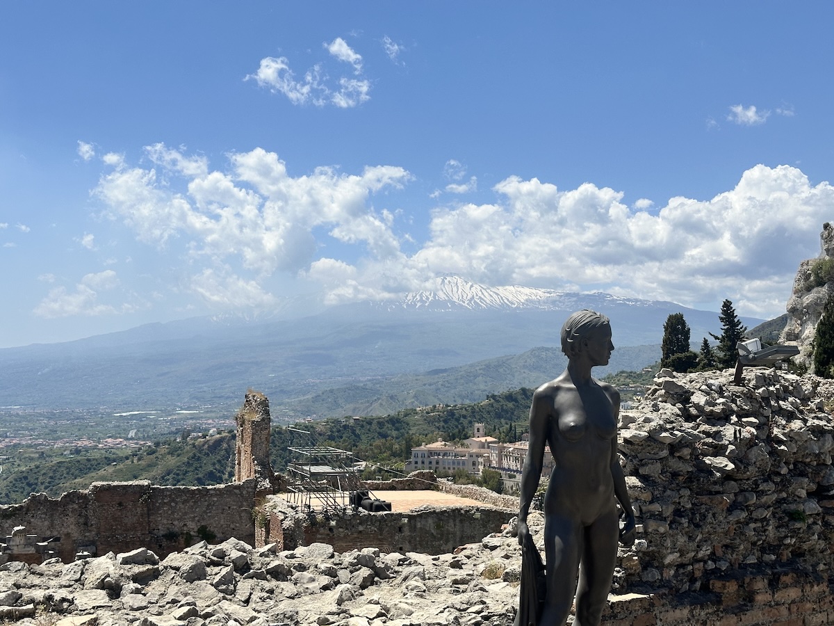 Von den Mauern des Teatro Antico Taormina reicht der Blick über das Tal bis zum schneebedeckten Ätna unter blauem Himmel.