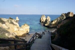 Steinerne Treppe hinab zu einer kleinen Bucht bei Lagos, umgeben von goldenen Felsen und blauem Atlantikwasser.