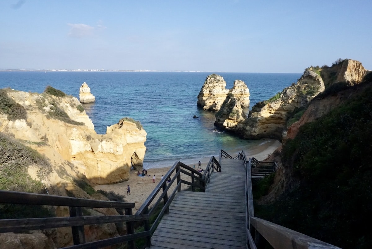 Steinerne Treppe hinab zu einer kleinen Bucht bei Lagos, umgeben von goldenen Felsen und blauem Atlantikwasser.
