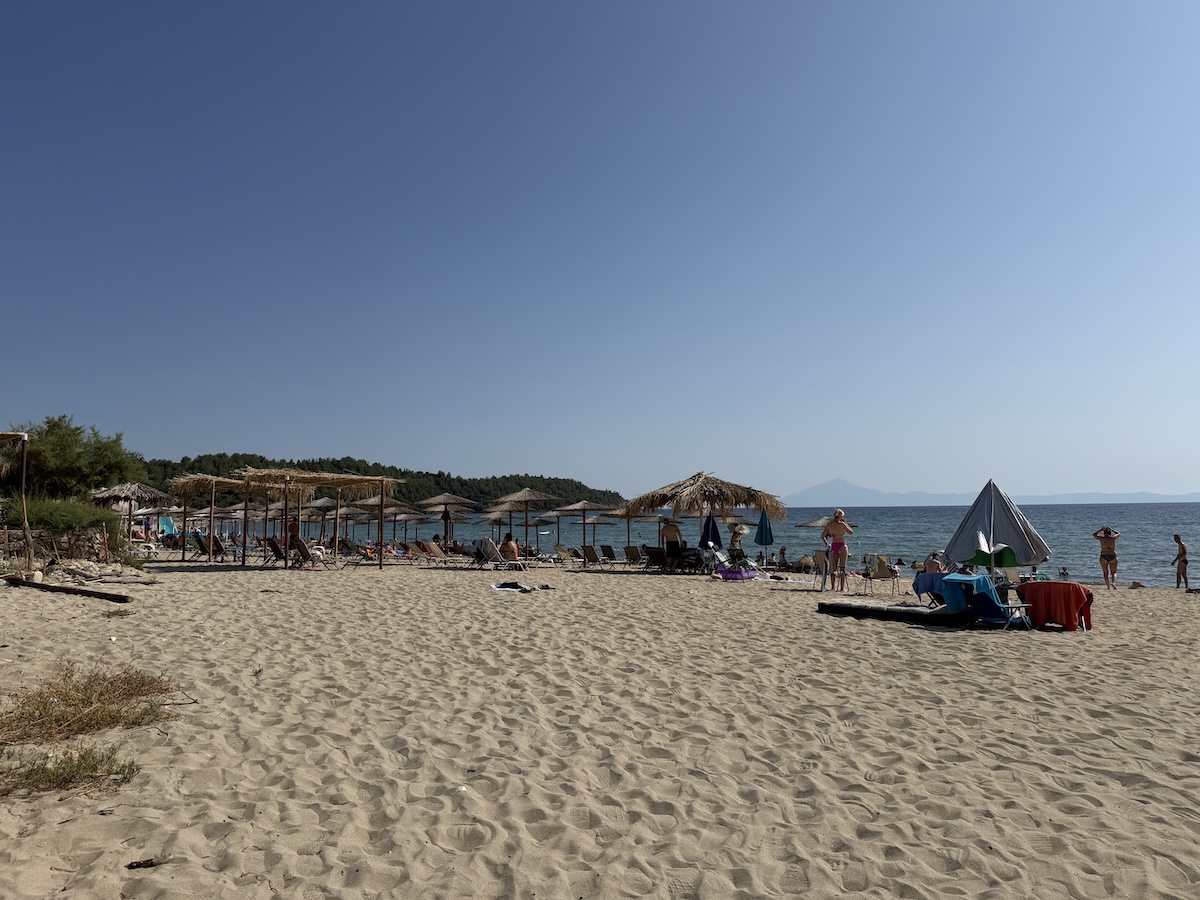 Breiter Sandstrand bei Potos auf Thassos mit Liegen, Sonnenschirmen und ruhigem Meer vor bewaldeten Hügeln